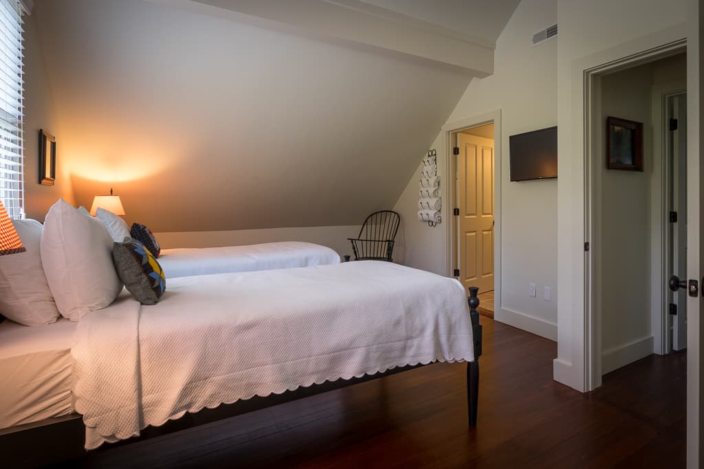 Cozy bedroom featuring two beds, warm lighting, and a sloped ceiling.