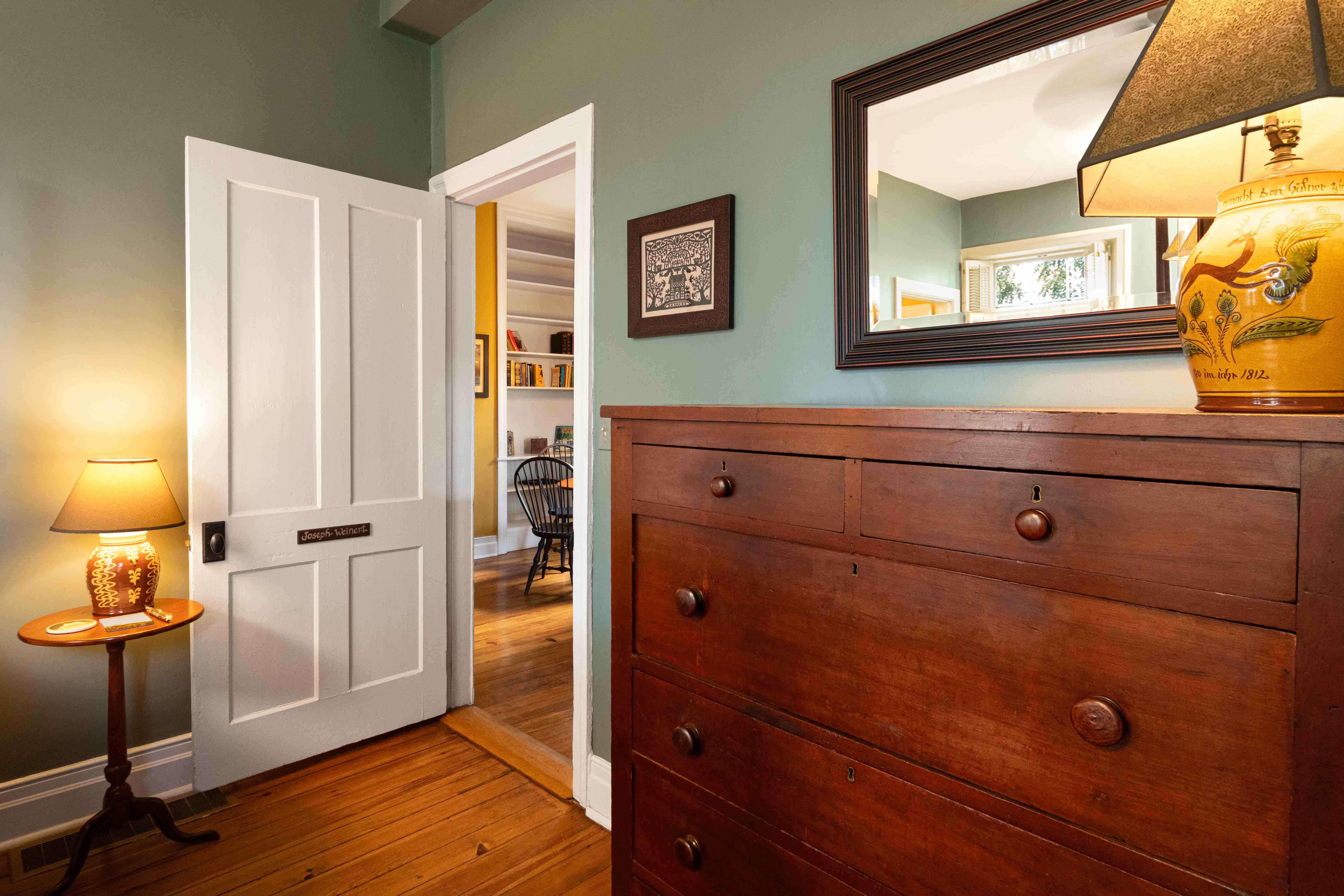 A wooden dresser and lamp in a bedroom with a doorway leading to another room.