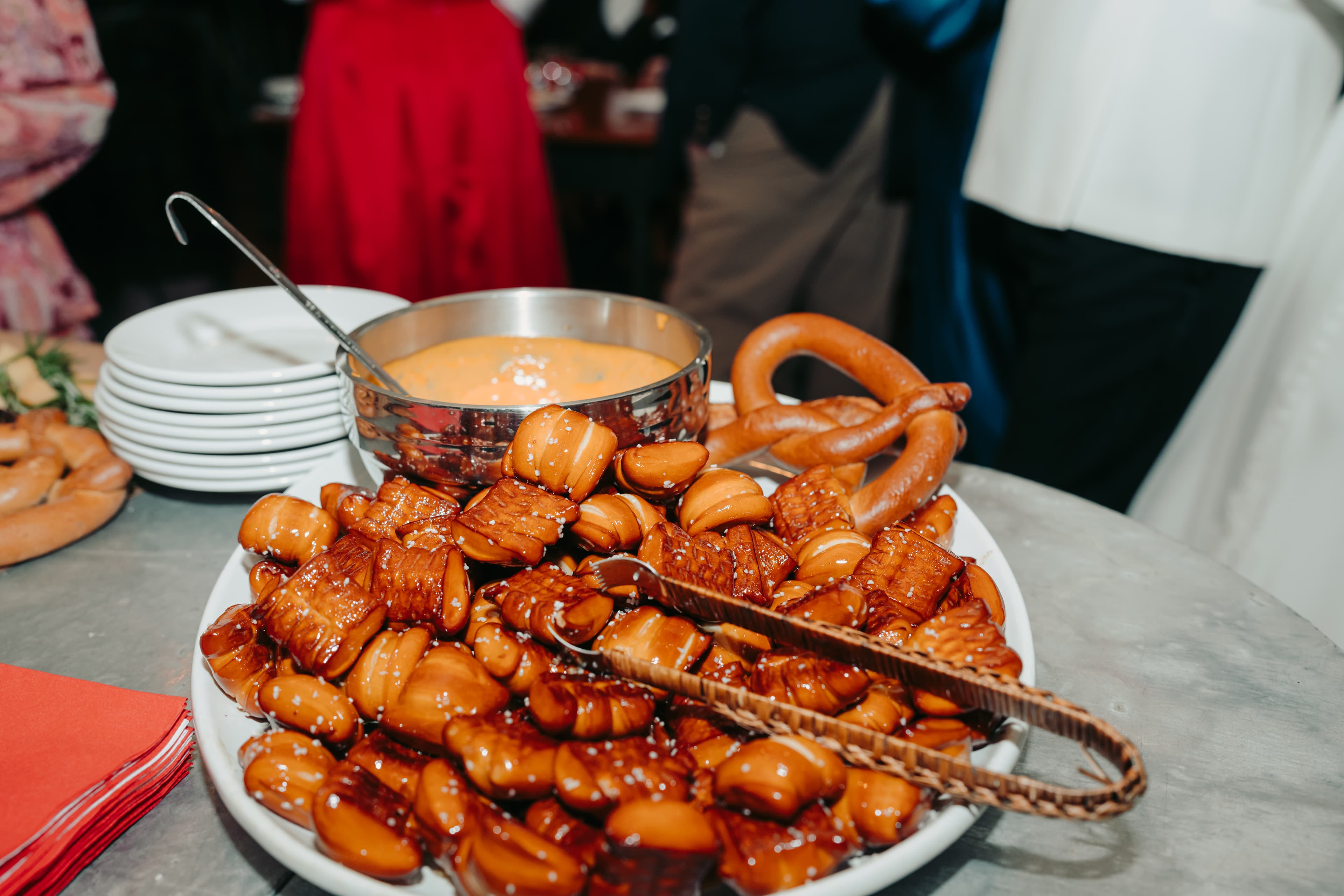 A platter of glazed pastries next to a bowl of dipping sauce and a pretzel.