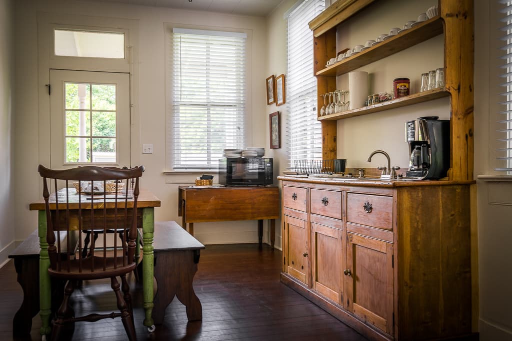 A cozy kitchen nook featuring a wooden table, chairs, and a coffee station with shelving.