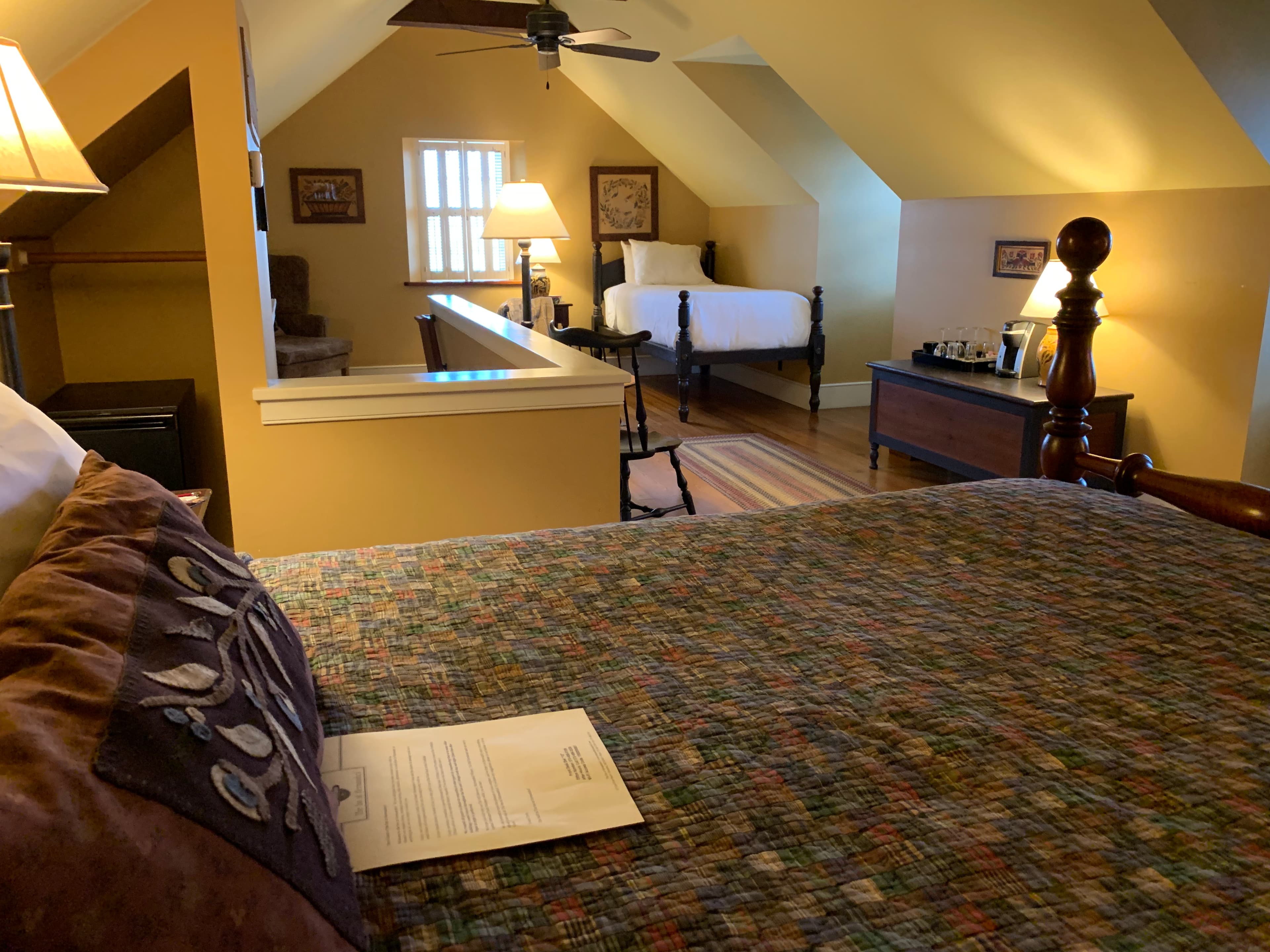 Cozy attic bedroom featuring a quilted bed, lamps, and a second bed in the background.