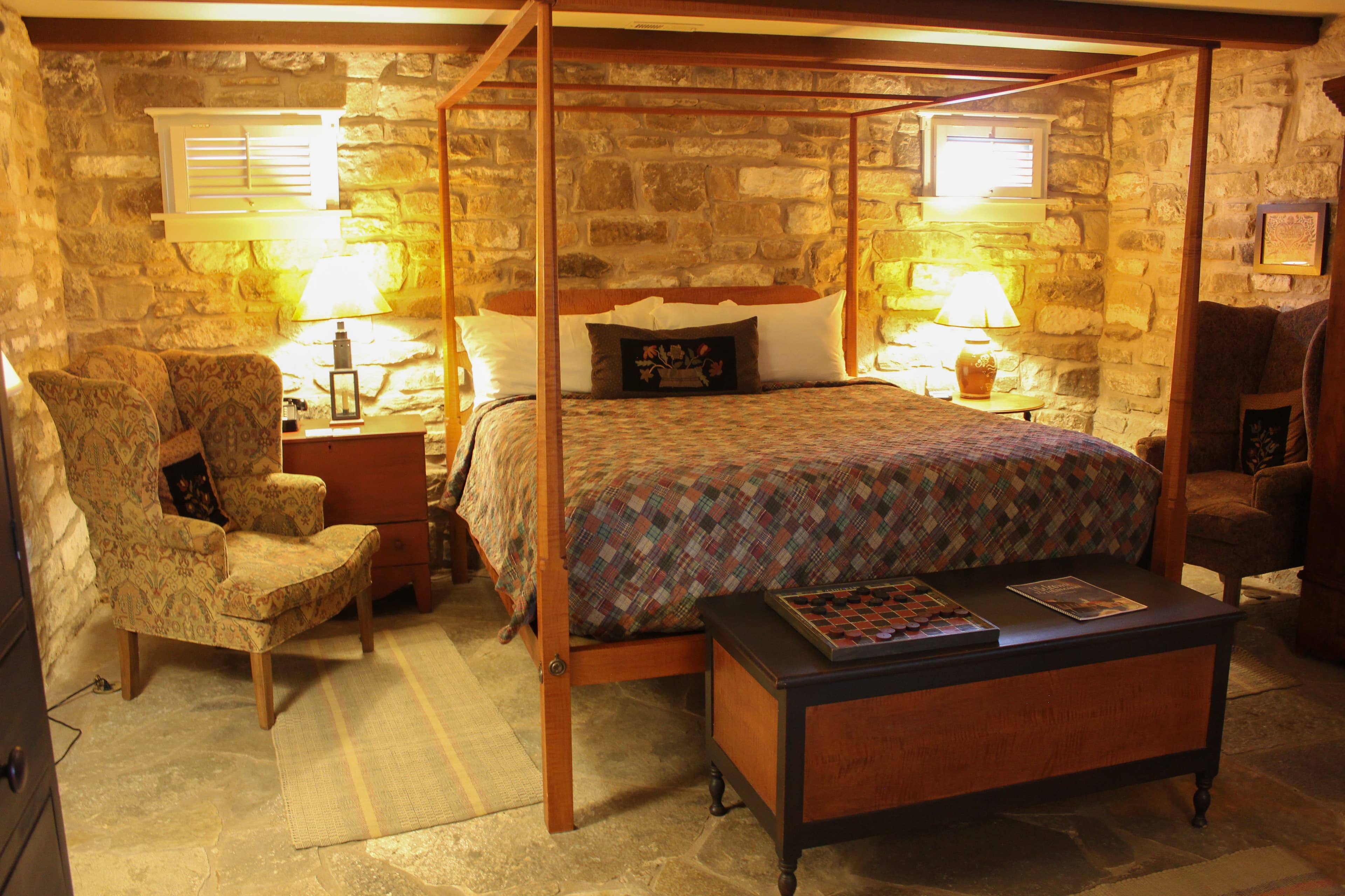 Cozy bedroom featuring a four-poster bed, patterned bedding, and stone walls with warm lighting.