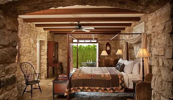 A cozy bedroom featuring stone walls, a four-poster bed, and a rustic wooden chair.