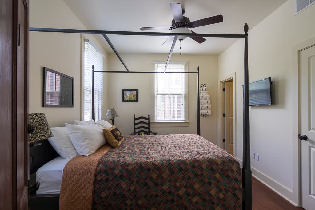 A cozy bedroom featuring a four-poster bed, quilted cover, and natural light from windows.