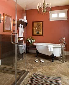 A stylish bathroom featuring a freestanding bathtub, glass shower, and warm orange walls.