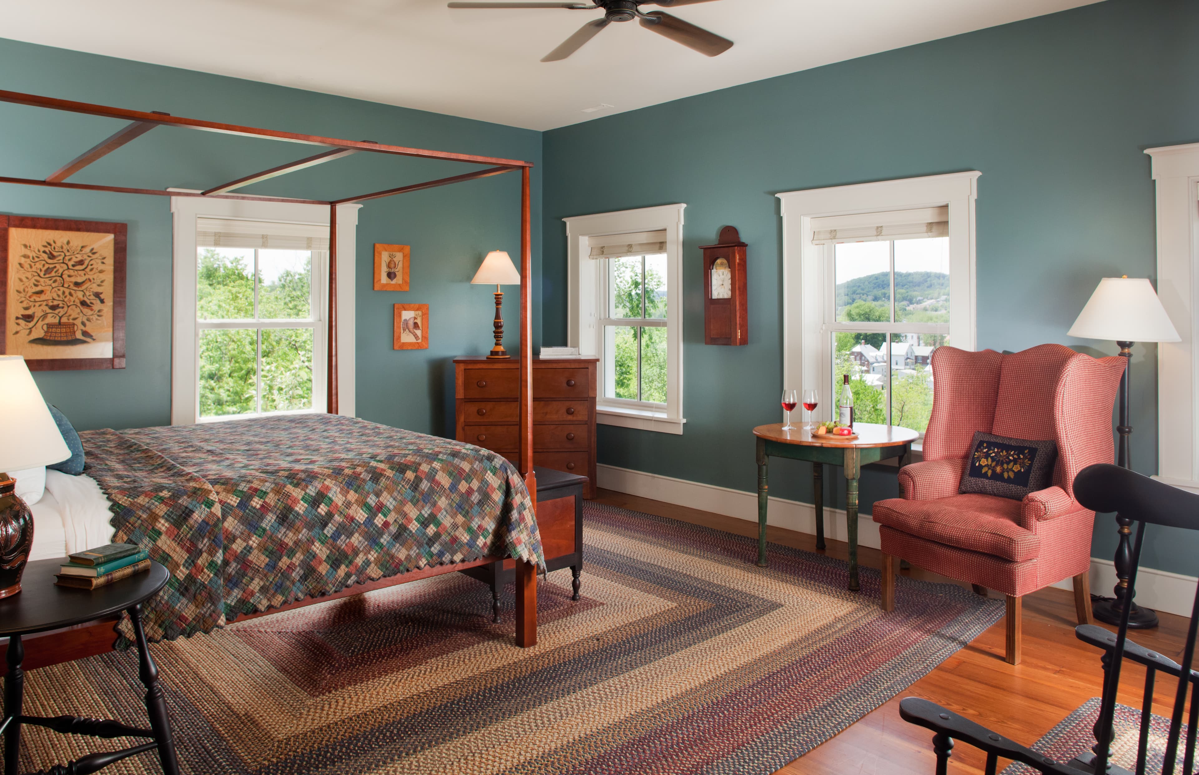 Cozy bedroom featuring a quilted bed, a rustic dresser, and a comfortable armchair against a teal wall.