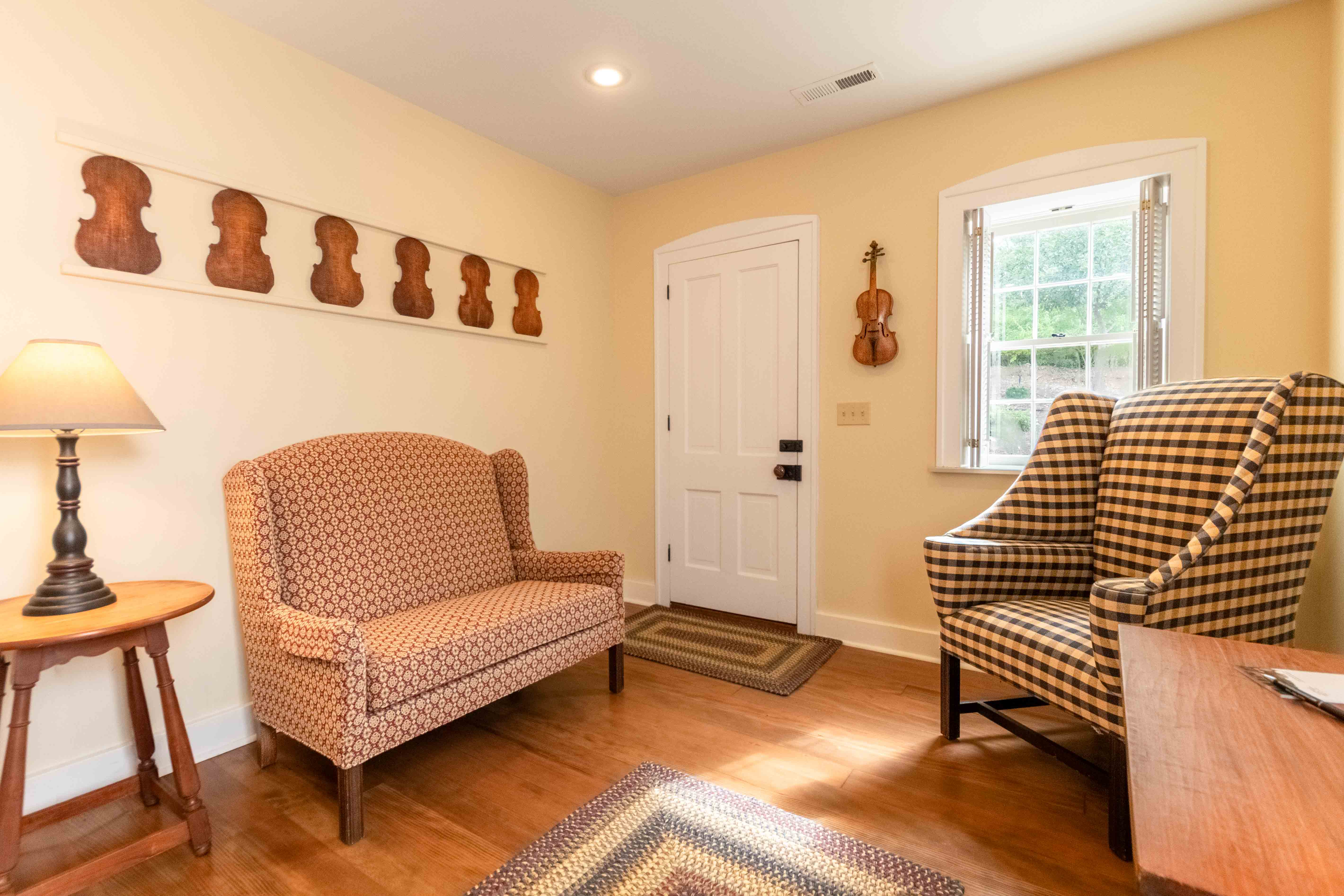 A cozy entryway featuring two patterned armchairs, a wooden table lamp, and a wall of violin-shaped decor.