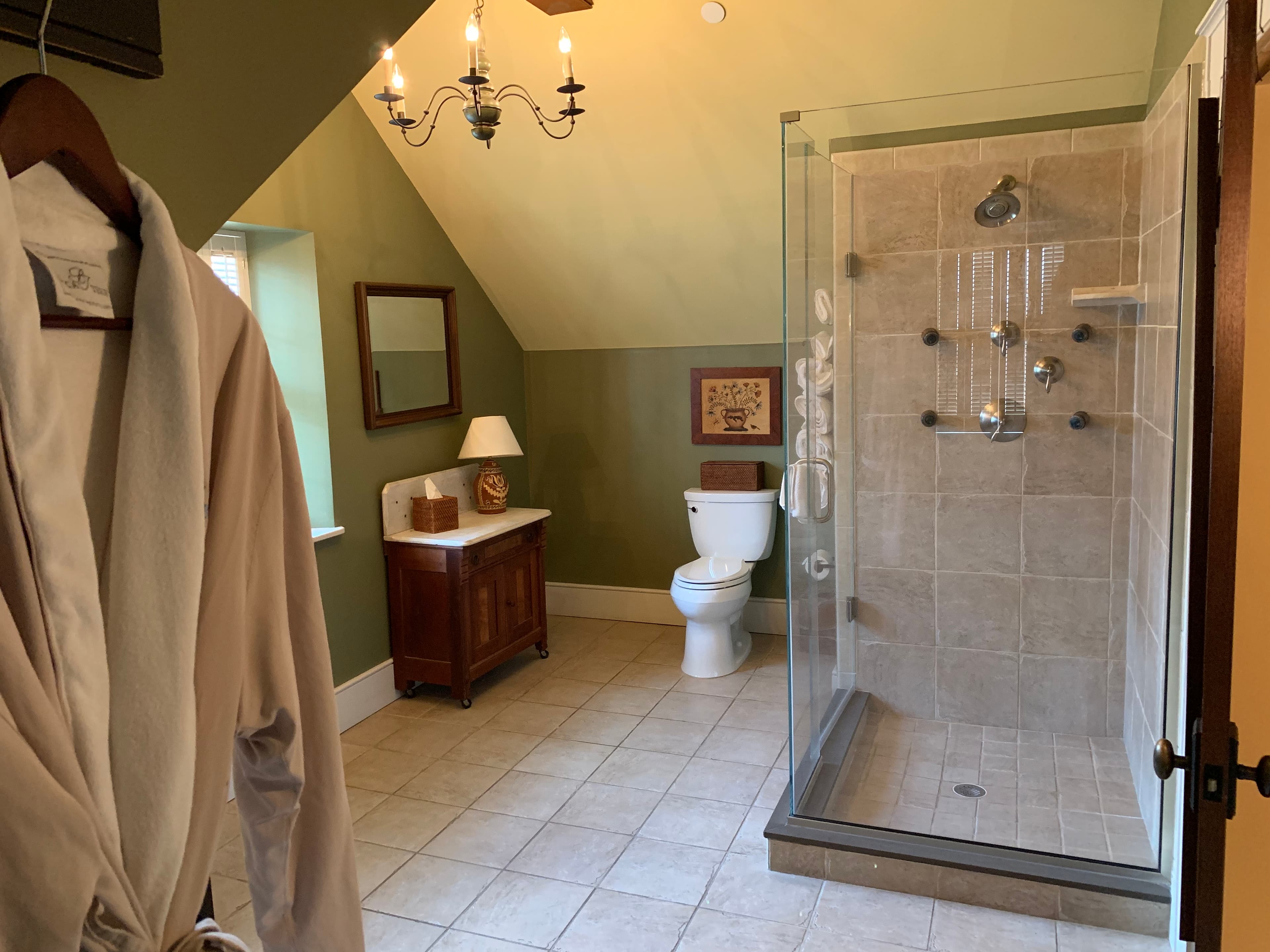 A spacious bathroom featuring a shower, toilet, and a robe hanging on the door.