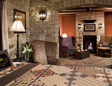 A cozy bedroom with a stone fireplace, patterned quilt, and comfortable seating areas.