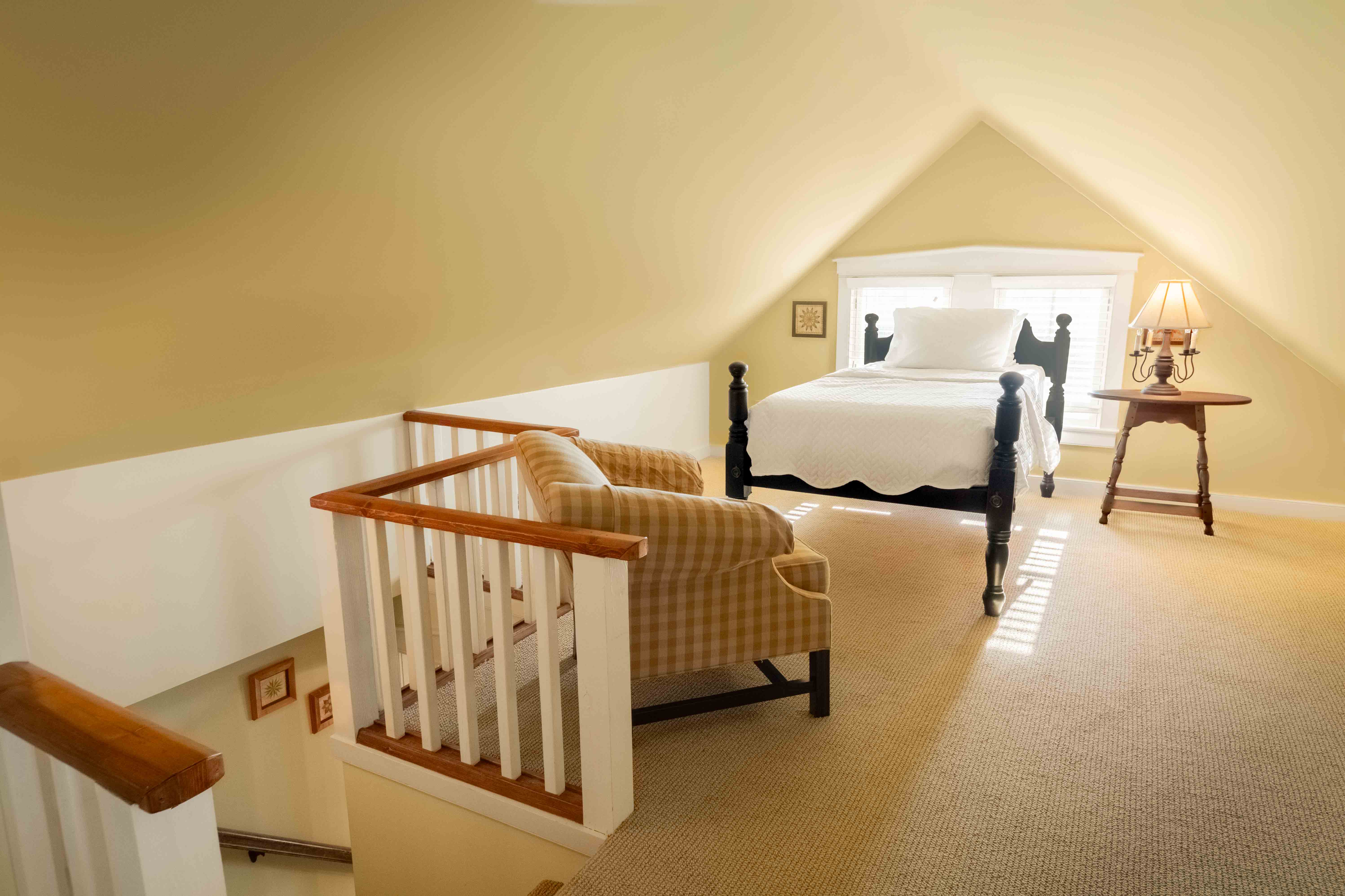 Cozy attic bedroom with a bed, armchair, and warm lighting.