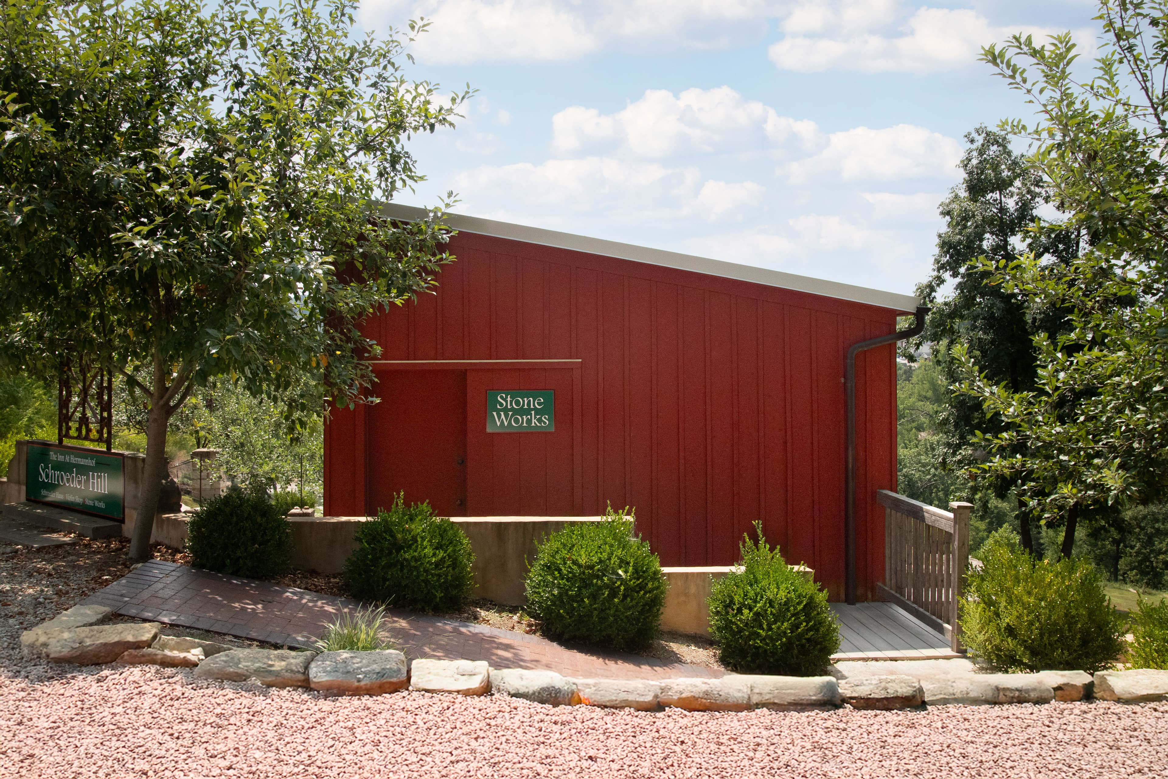 A red building with a sign reading "Stone Works" is surrounded by greenery and stone pathways under a partly cloudy sky.