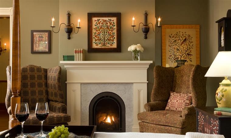 Cozy sitting area with two armchairs, a fireplace, and elegant decor, featuring wine glasses and a vase of flowers.