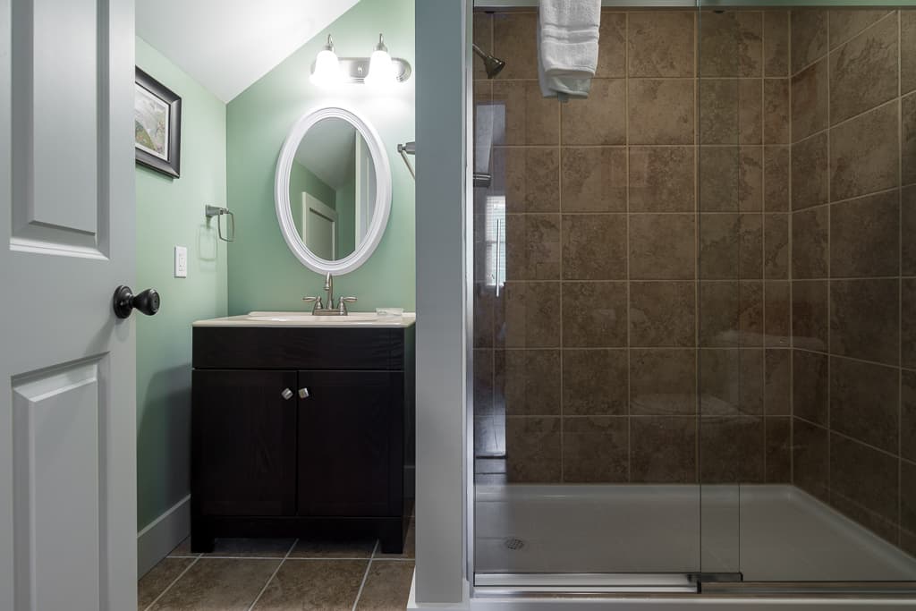 A modern bathroom featuring a dark wooden vanity, round mirror, and a glass shower enclosure with tiled walls.