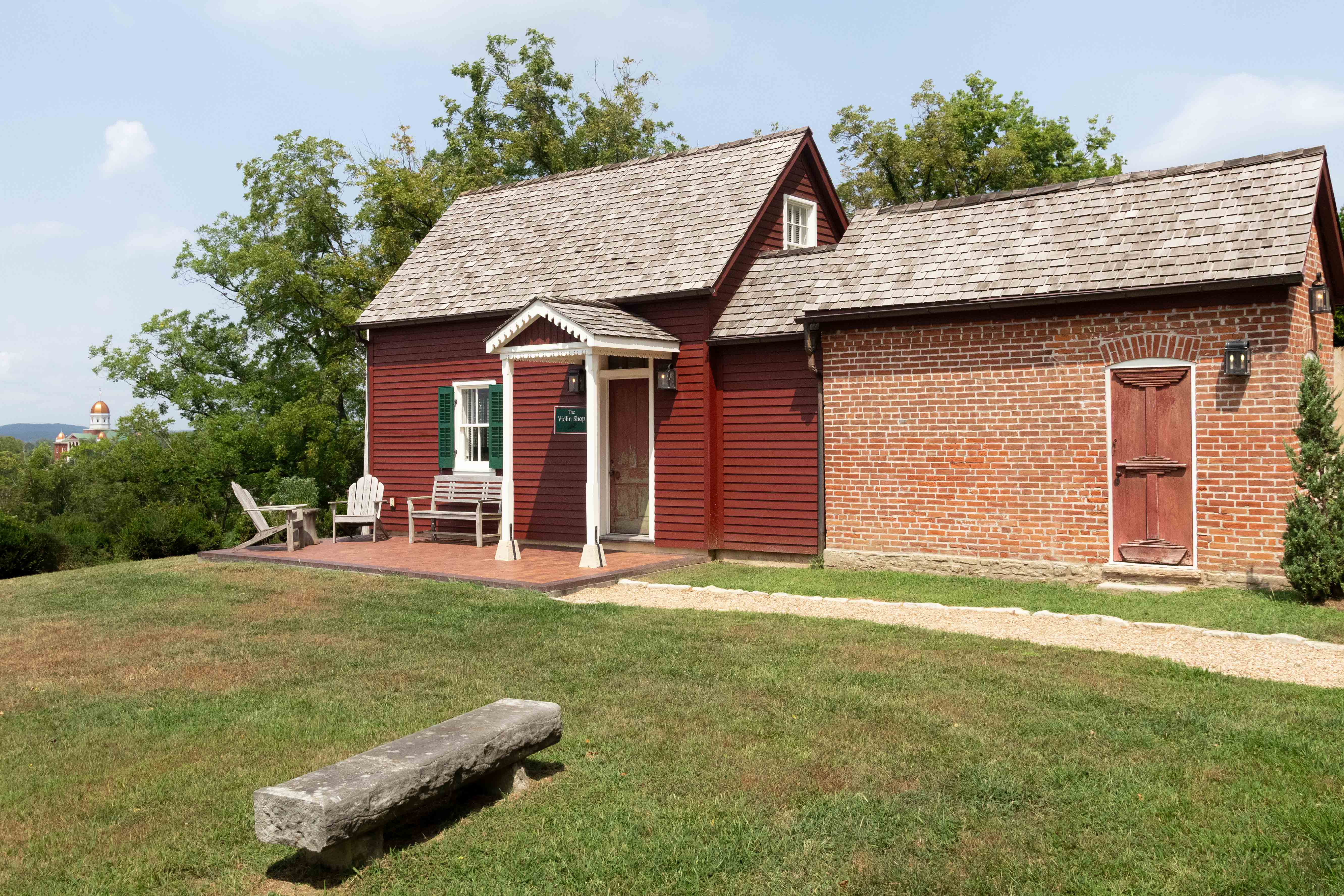 A red building with a wooden porch and a shingled roof, set on grassy terrain.