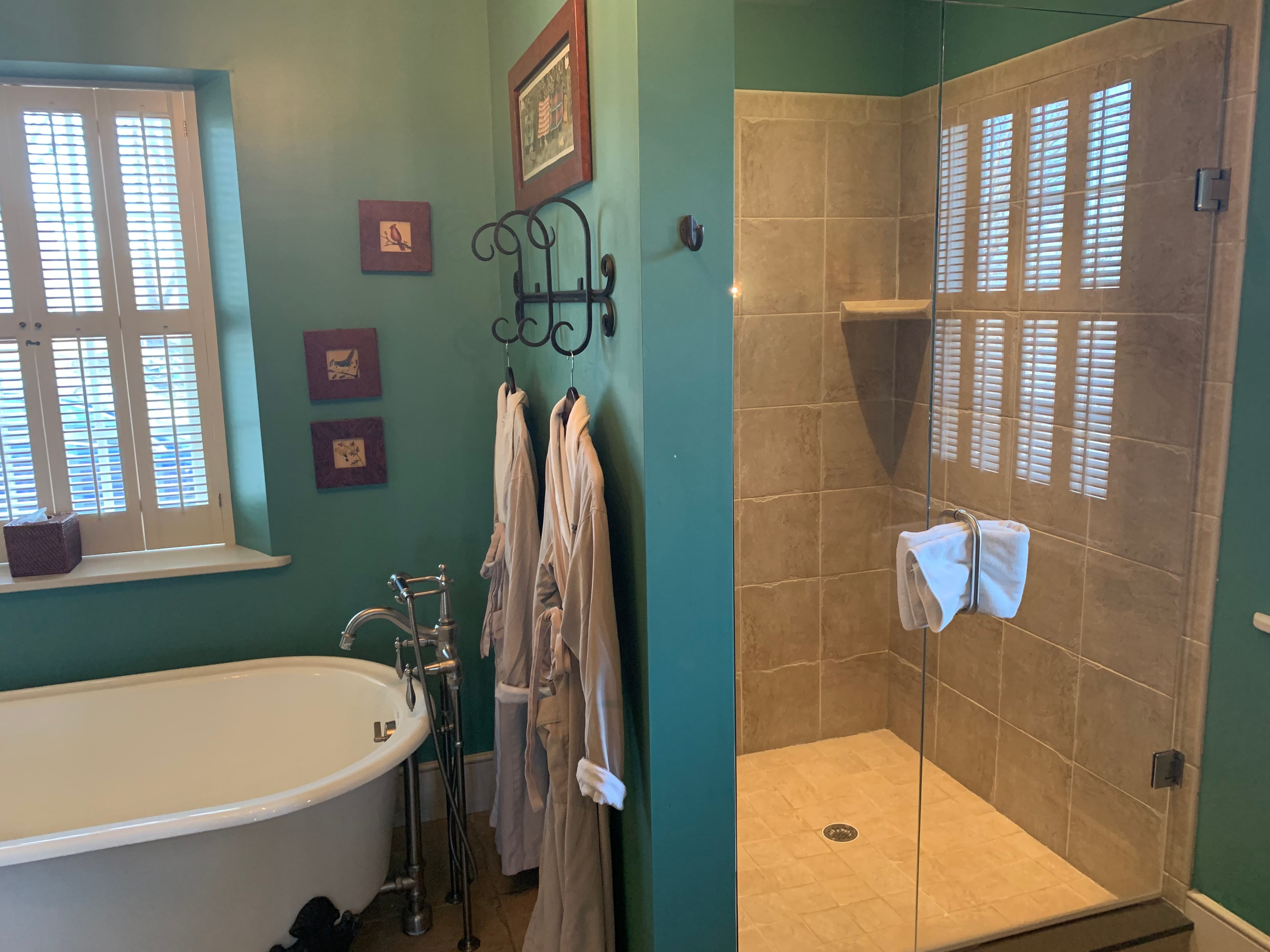 A stylish bathroom featuring a freestanding bathtub, a glass shower, and plush robes hanging on the wall.