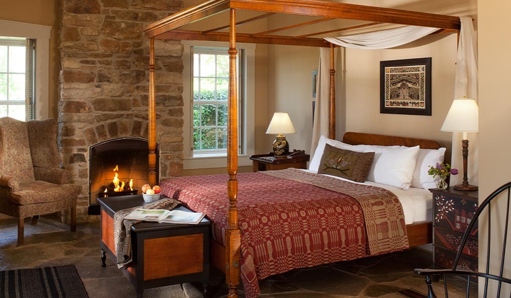 A cozy bedroom featuring a four-poster bed, a stone fireplace, and comfortable seating.