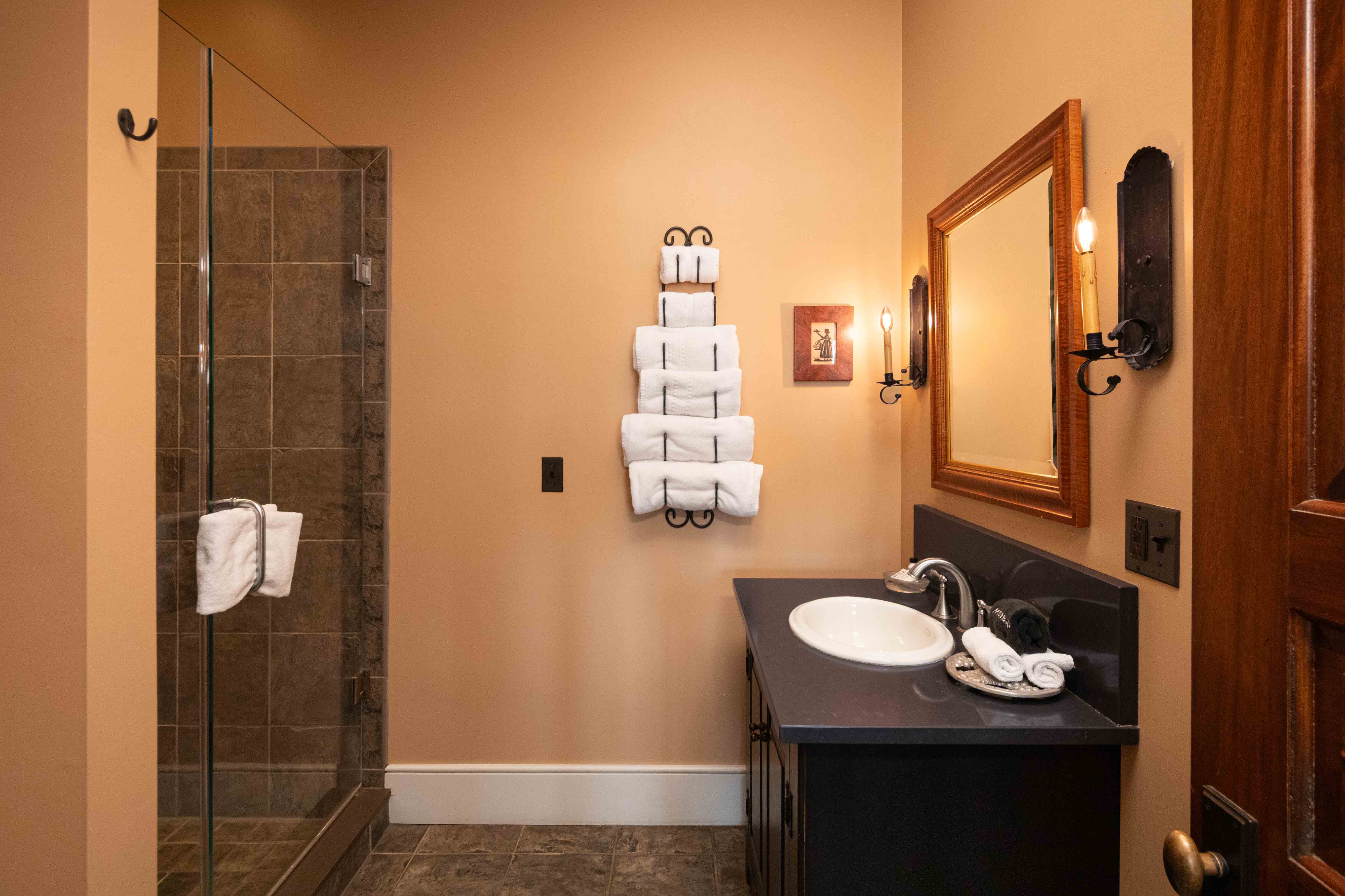 A modern bathroom featuring a glass shower, a dark vanity with a sink, and neatly arranged white towels on the wall.