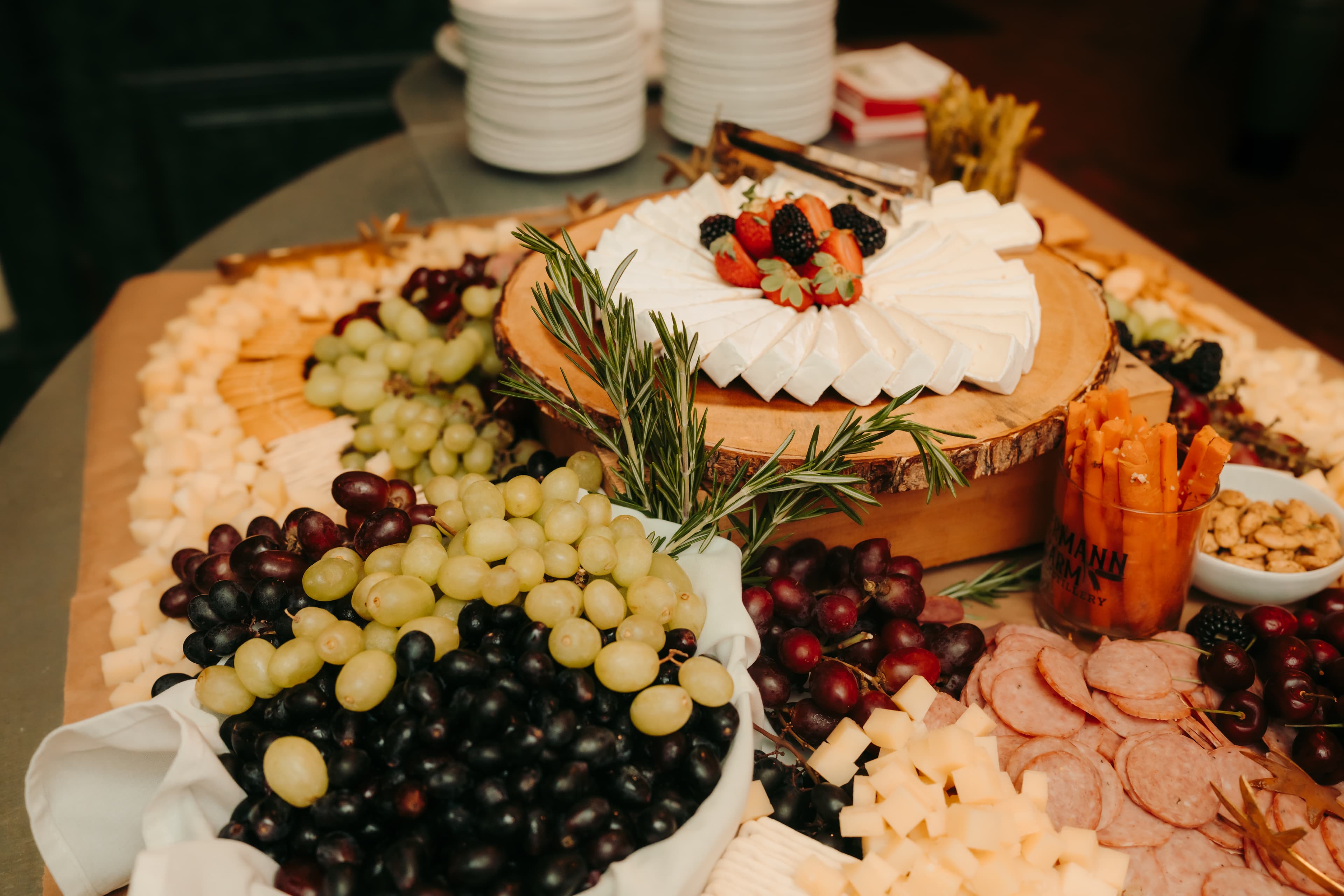 A beautifully arranged cheese and charcuterie platter featuring various cheeses, grapes, cured meats, nuts, and a cake adorned with berries.