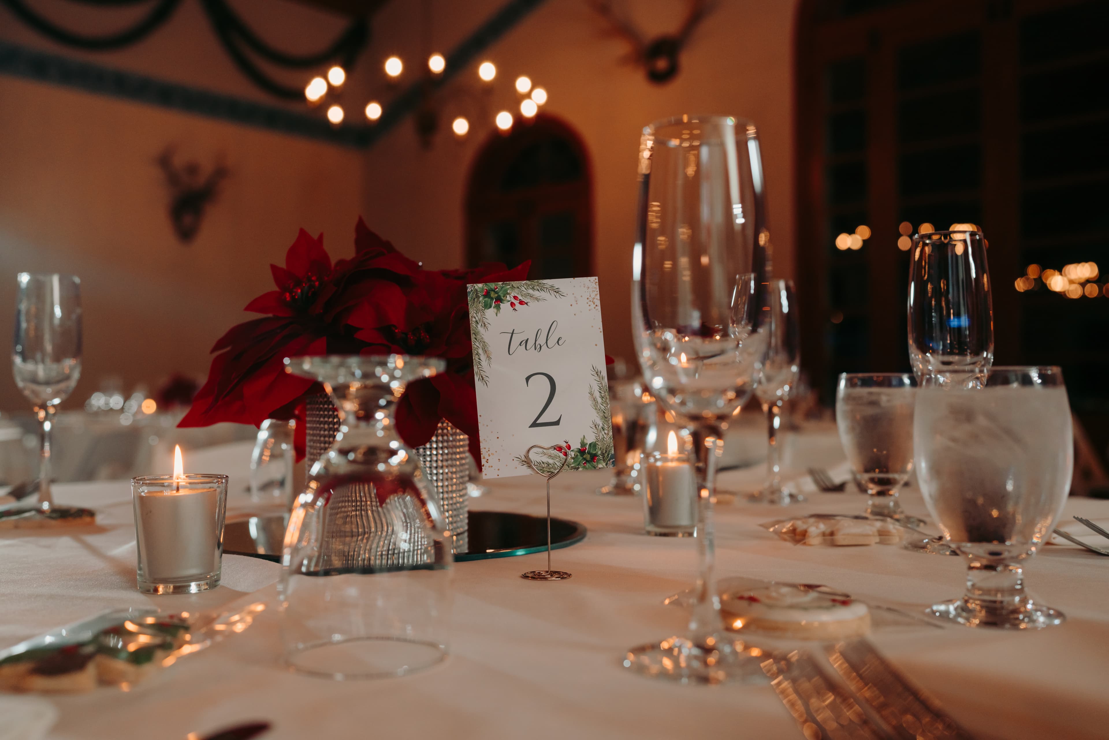 A beautifully set dining table with candles, glassware, and a centerpiece featuring a poinsettia and a sign indicating "Table 2."