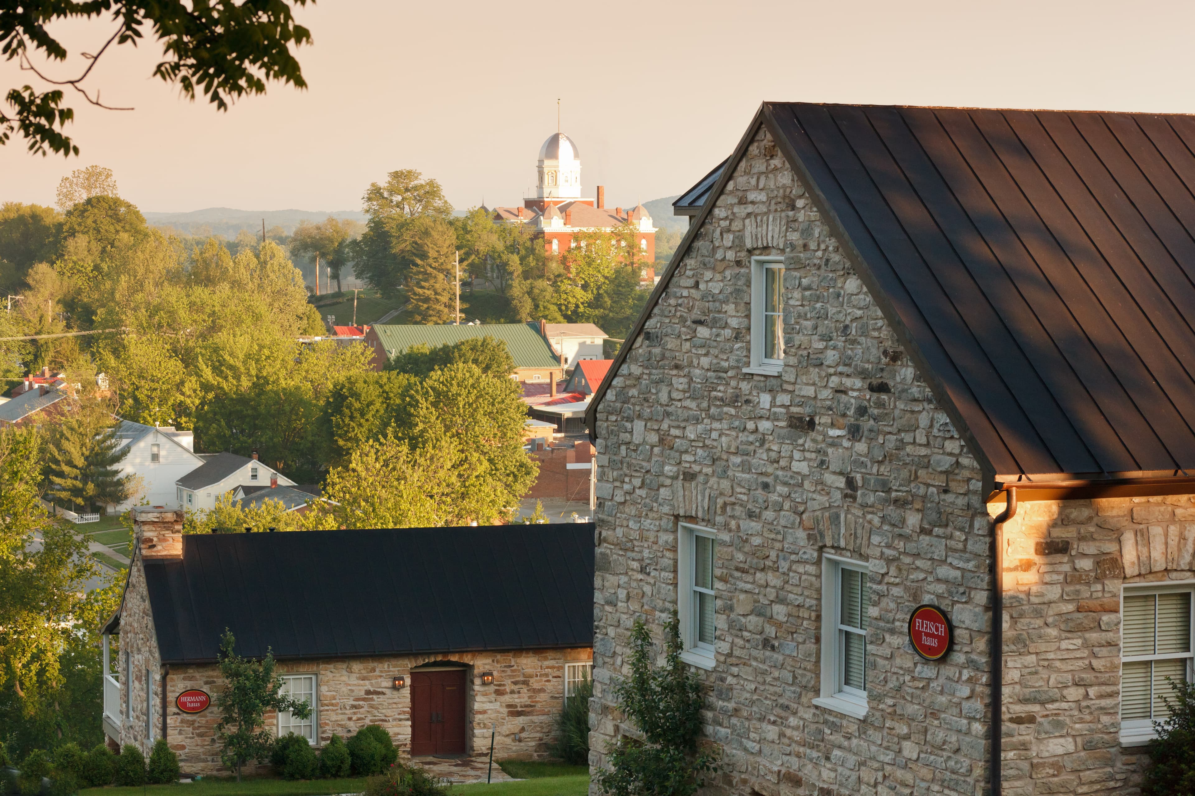 A serene view of a quaint town with stone houses nestled among lush greenery and distant buildings.