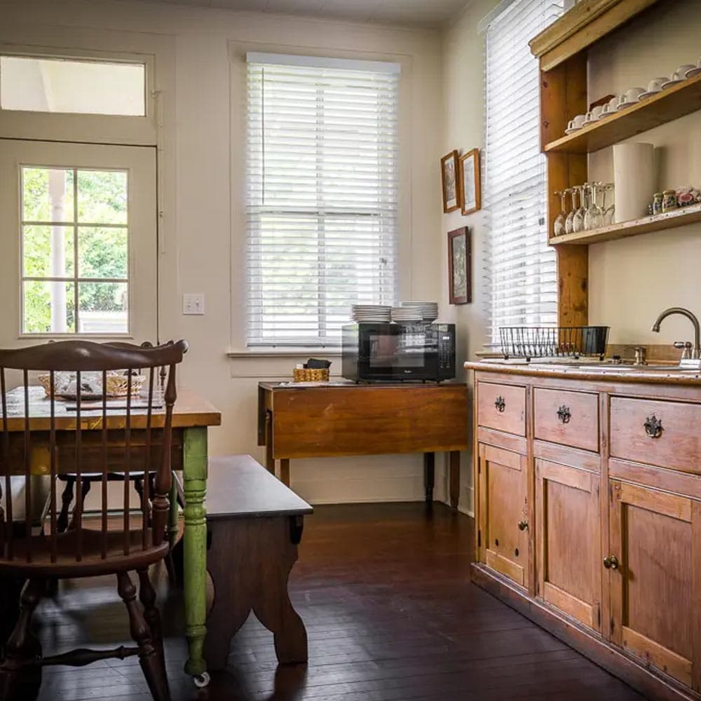 A cozy kitchen featuring wooden furniture, a microwave, and natural light from large windows.