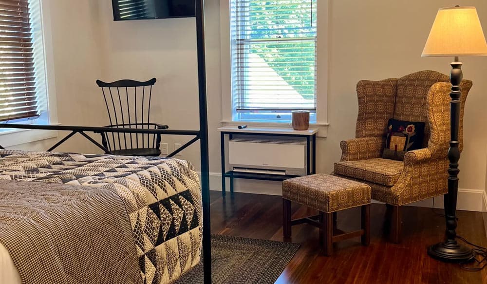 A cozy bedroom featuring a bed with a patterned quilt, a black rocking chair, a decorative armchair, and a small footstool.