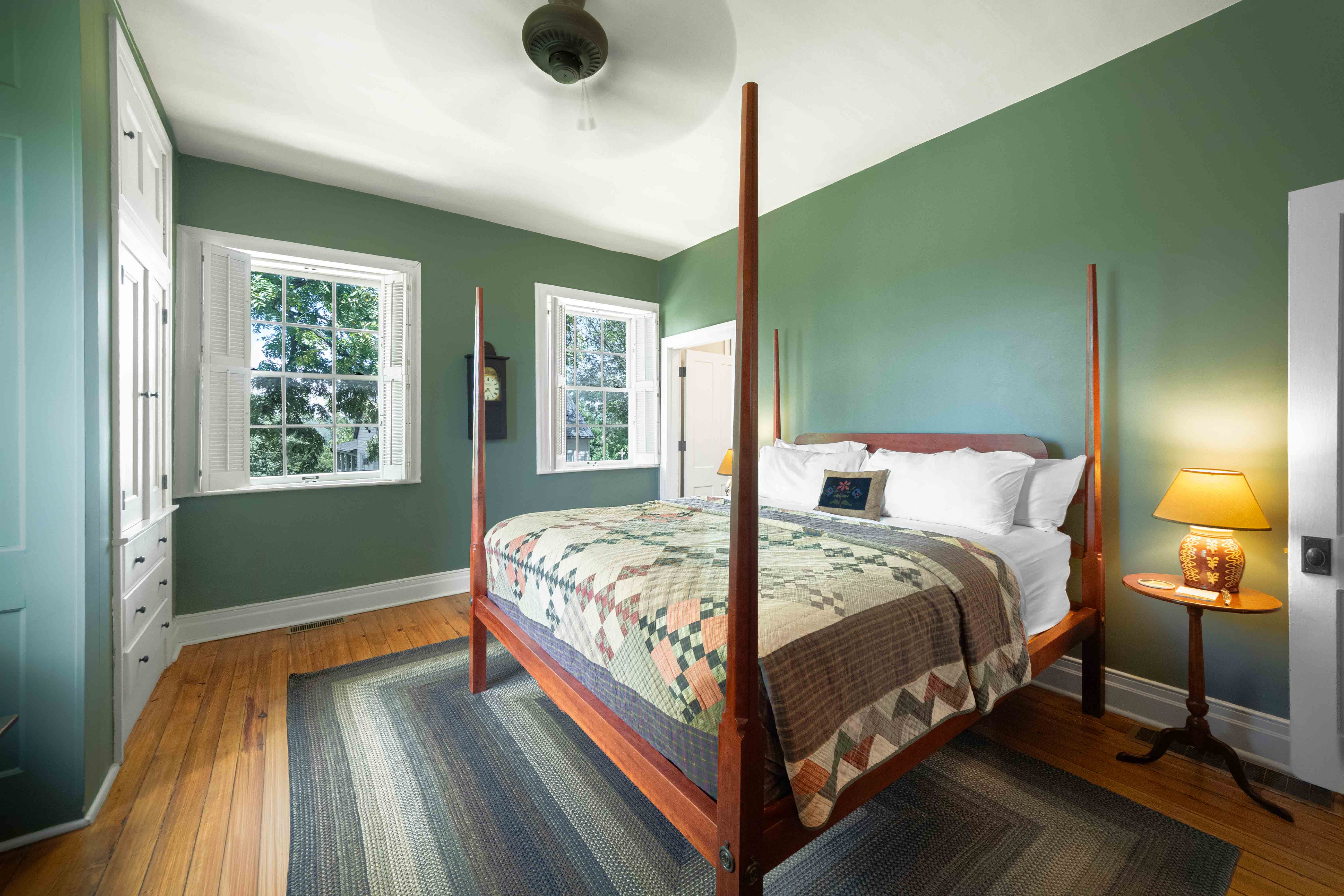 A cozy bedroom featuring a four-poster bed, green walls, and large windows.