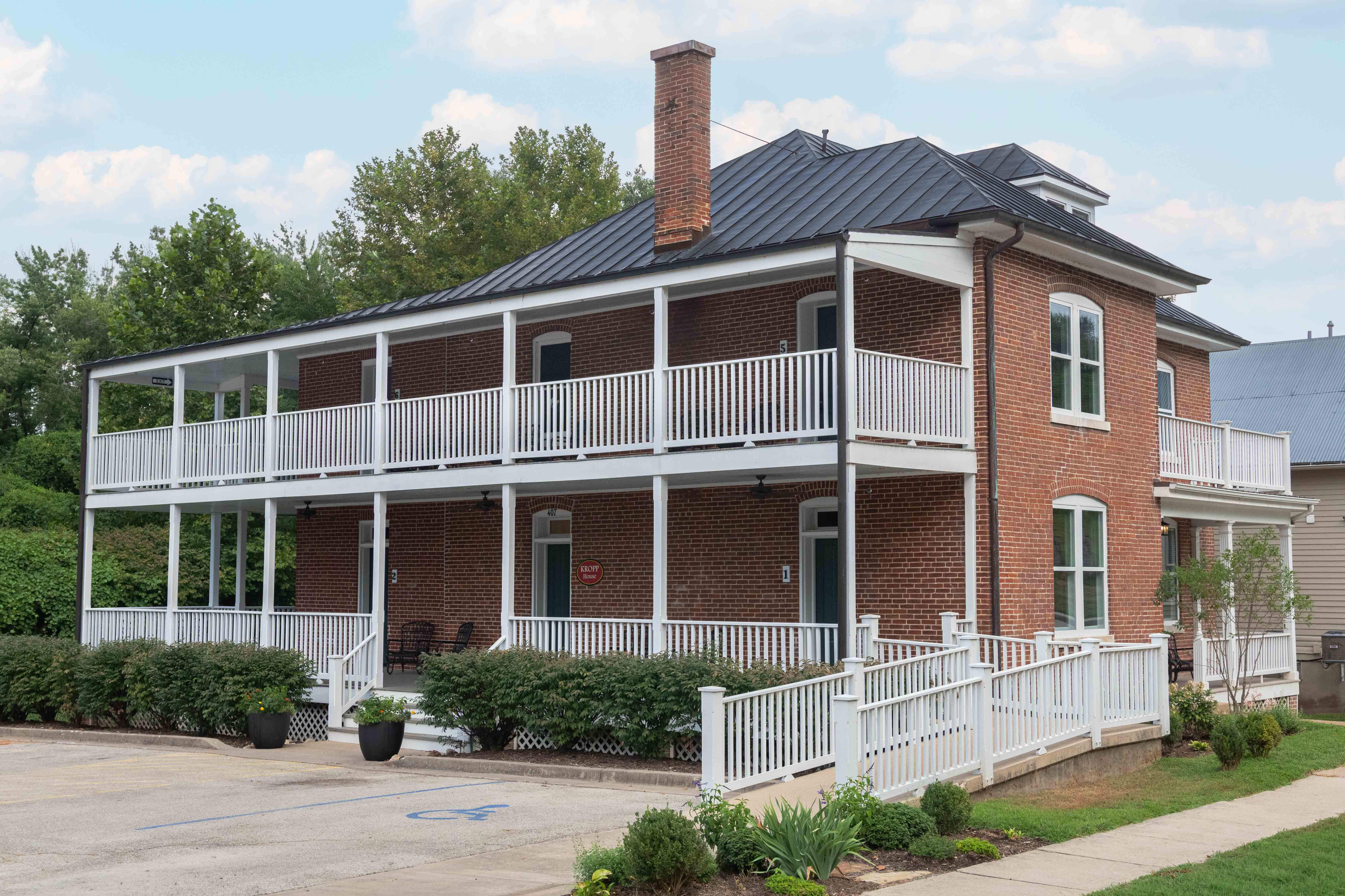 Two-story red brick house with a black metal roof and porches on both levels.