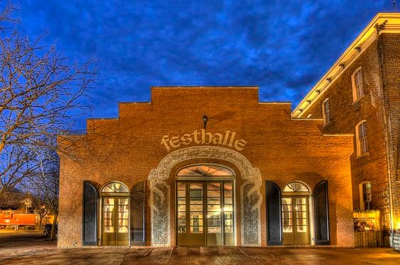 A brick building with large glass doors and "Festhalle" written above, set against a twilight sky.