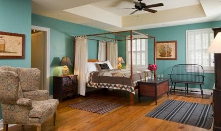A cozy bedroom featuring a four-poster bed, vintage seating, and teal walls.