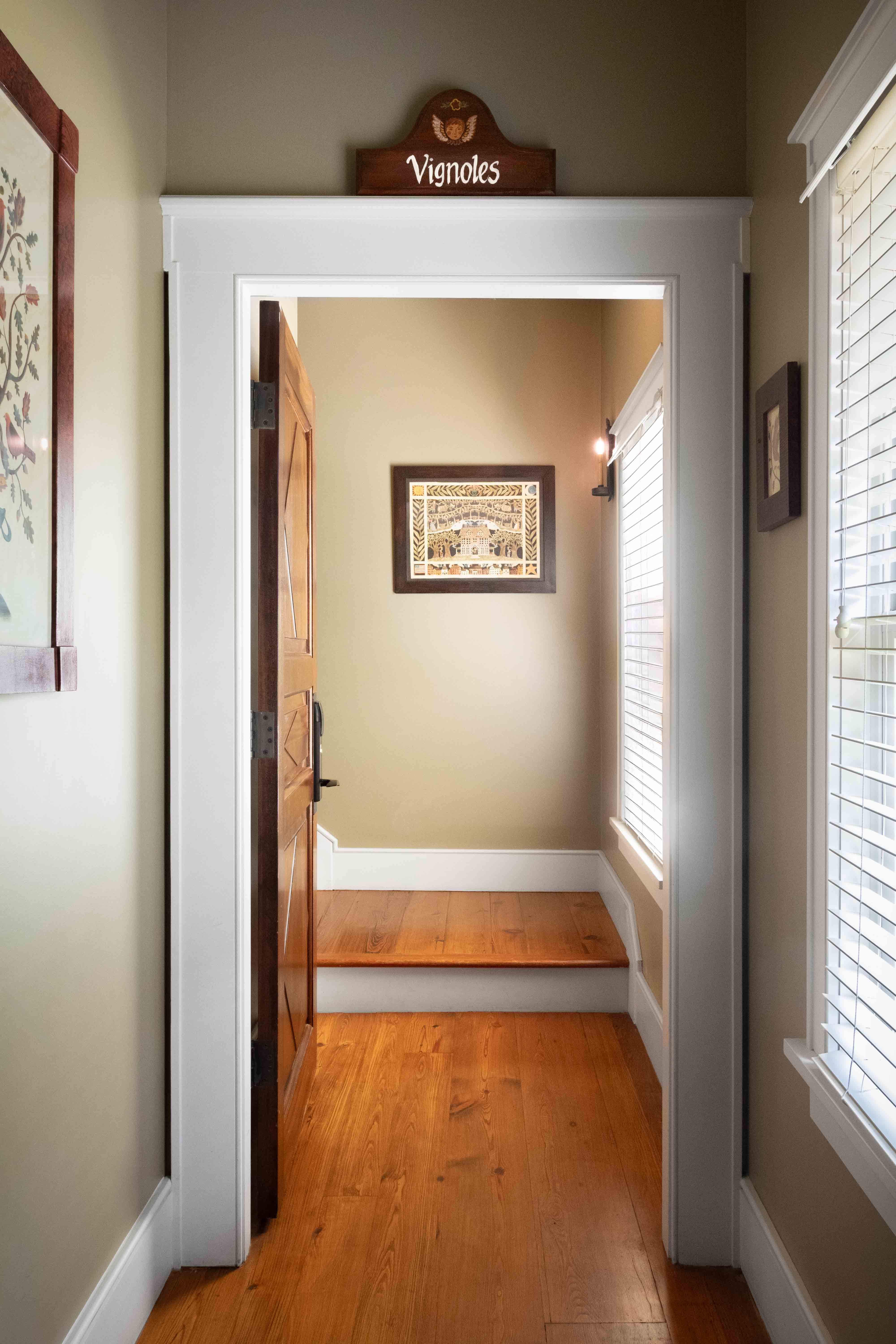 A doorway leads to a well-lit room with wood flooring, framed artwork, and a sign reading "Vignoles" above.