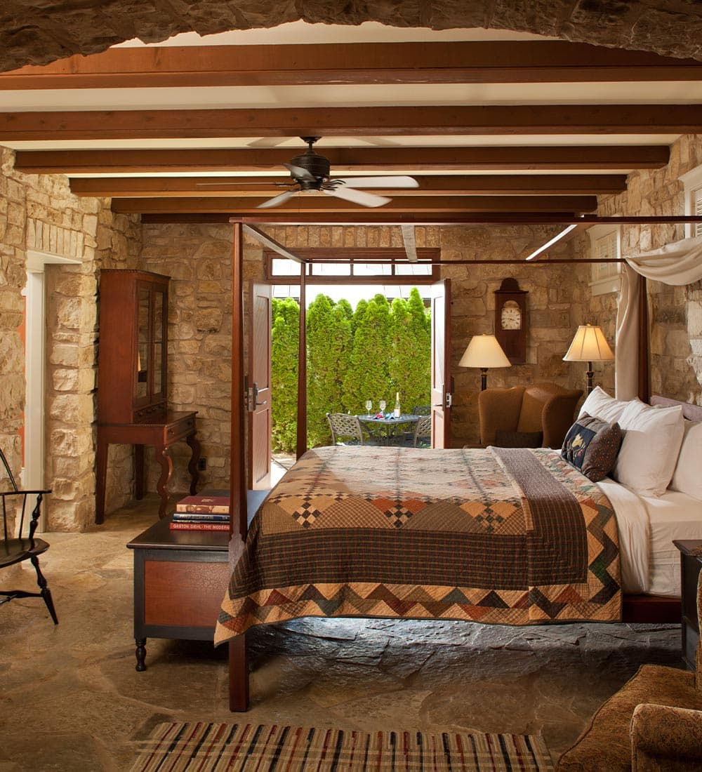 Cozy stone bedroom featuring a quilted bed, wooden furnishings, and access to a lush outdoor patio.