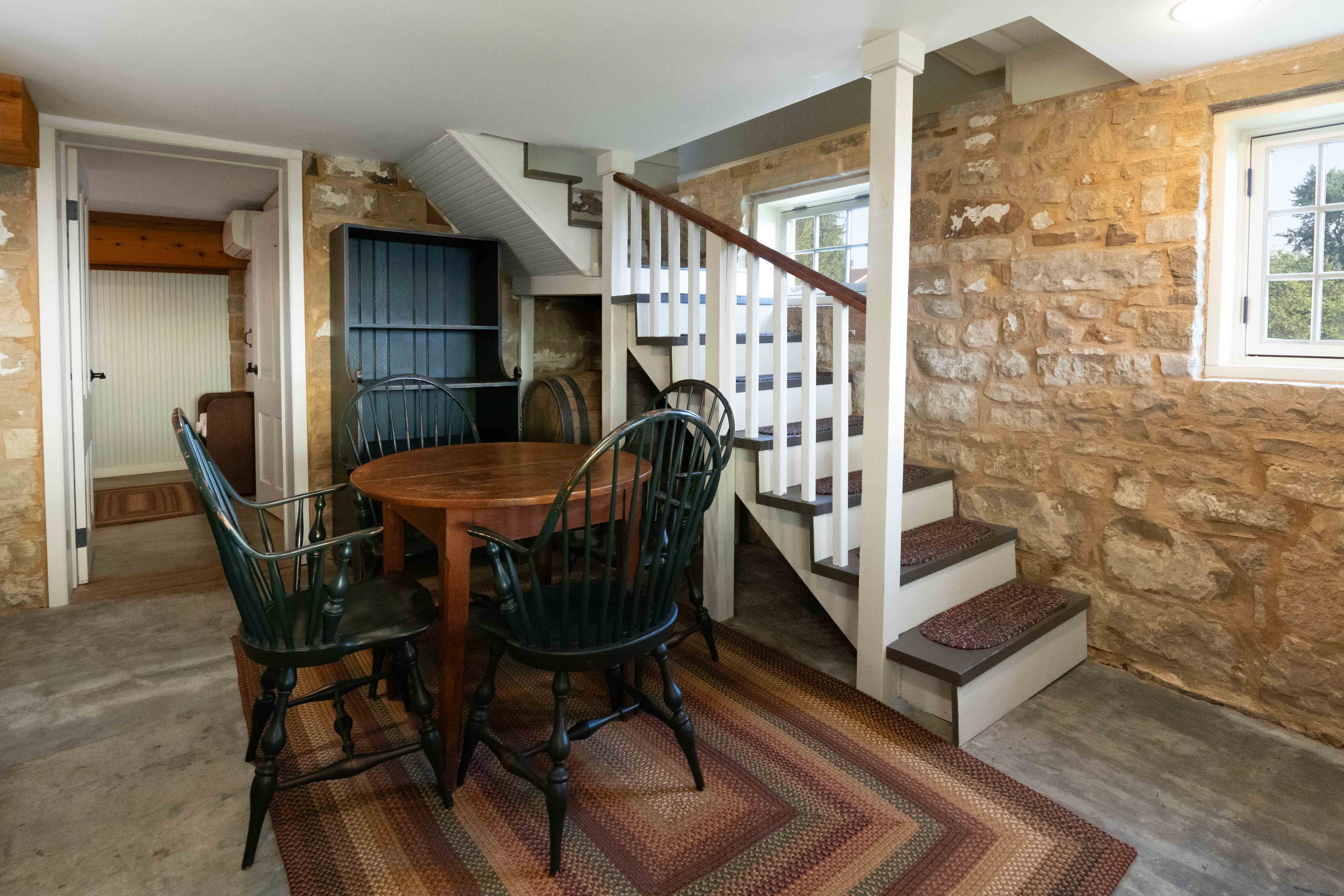 A cozy basement dining area features a round wooden table and green chairs, with a staircase leading to the upper floor.