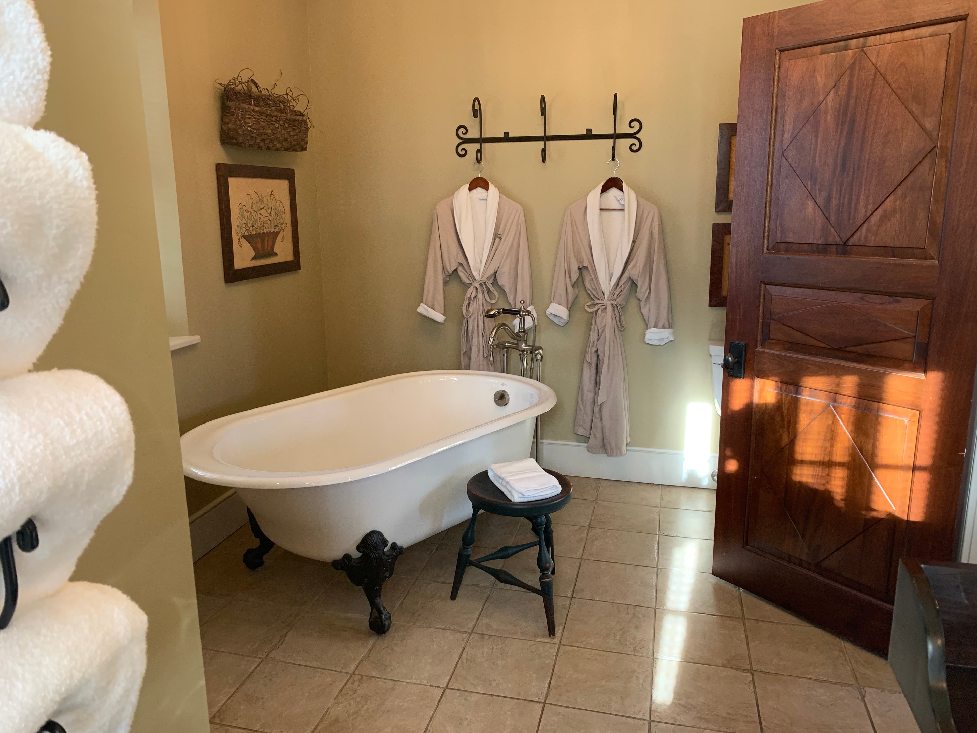 A cozy bathroom featuring a clawfoot tub, two hanging bathrobes, and a wooden door.