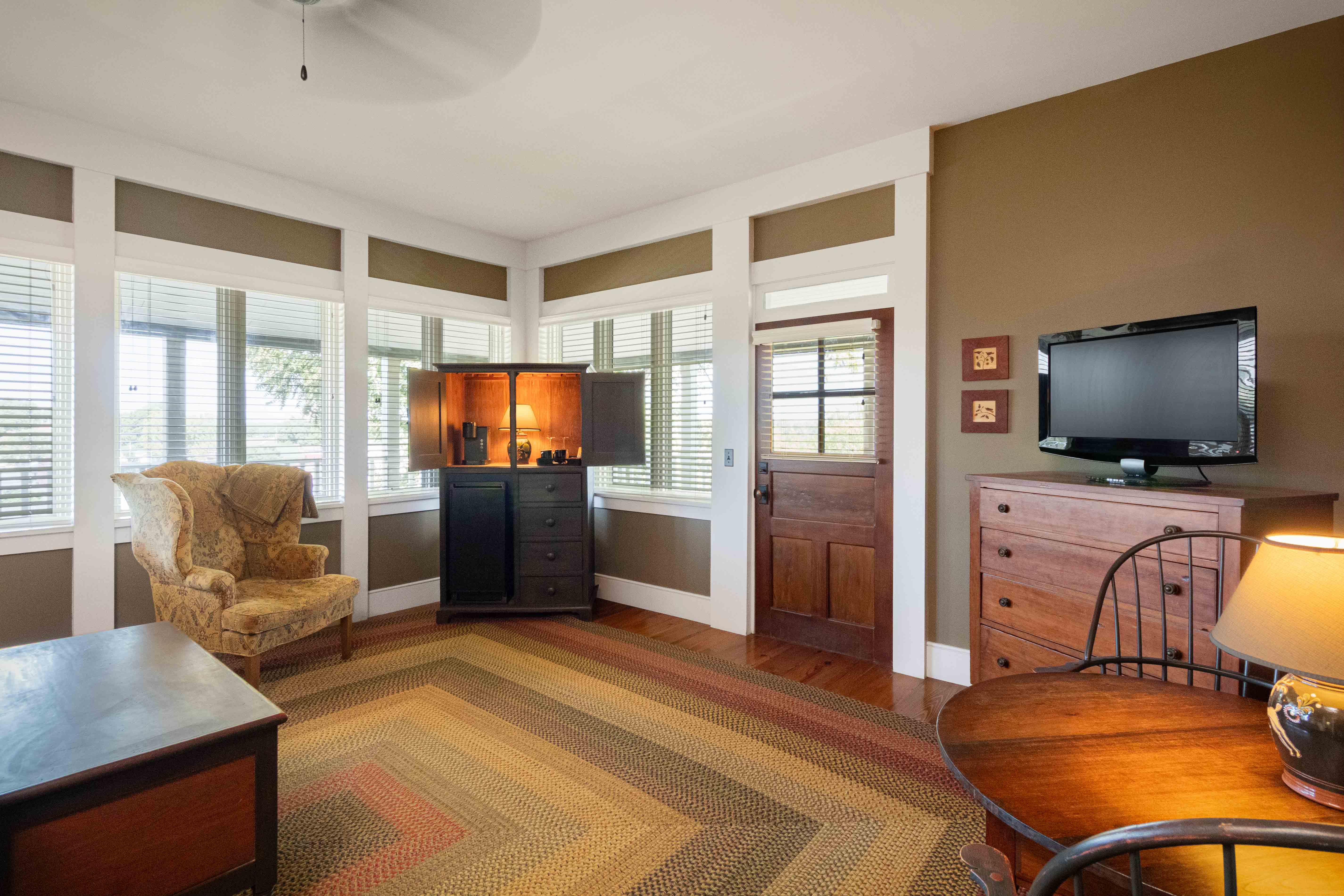 Cozy living room featuring a patterned rug, armchair, wooden furniture, and windows with natural light.