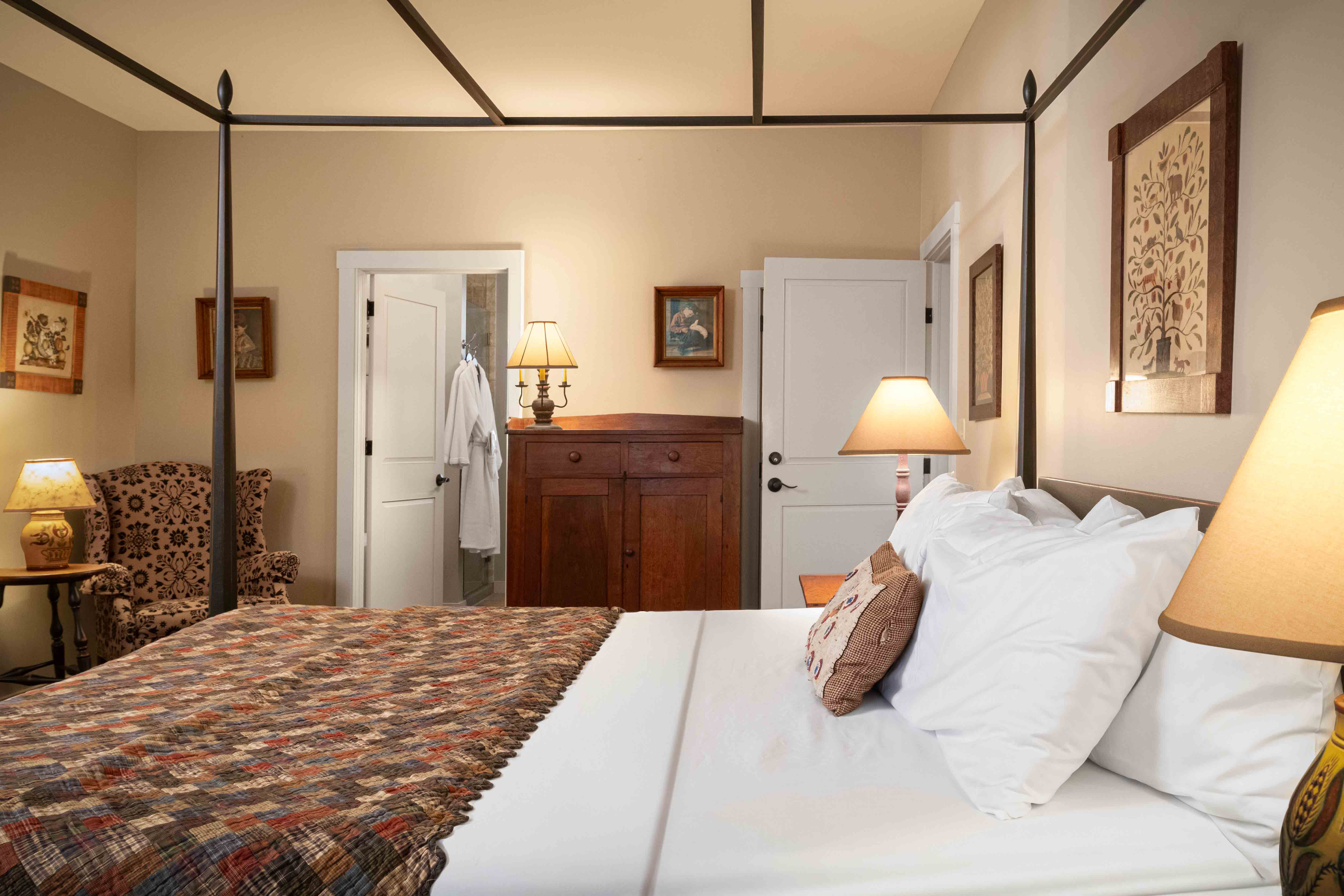 A cozy bedroom featuring a four-poster bed, patterned quilt, and warm lighting.