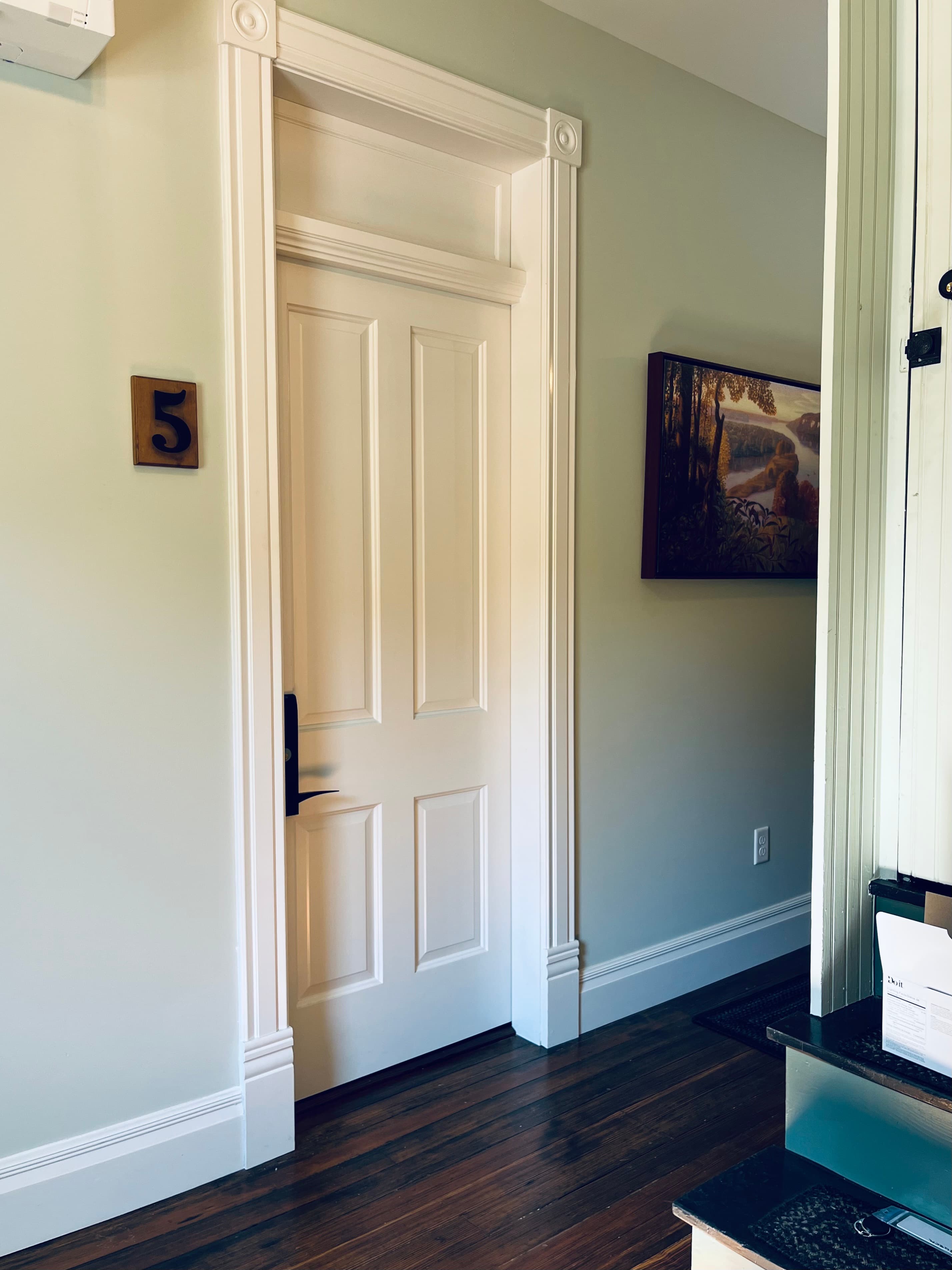 A closed white door with the number 5 on the wall beside it, framed by light green walls and a wooden floor.