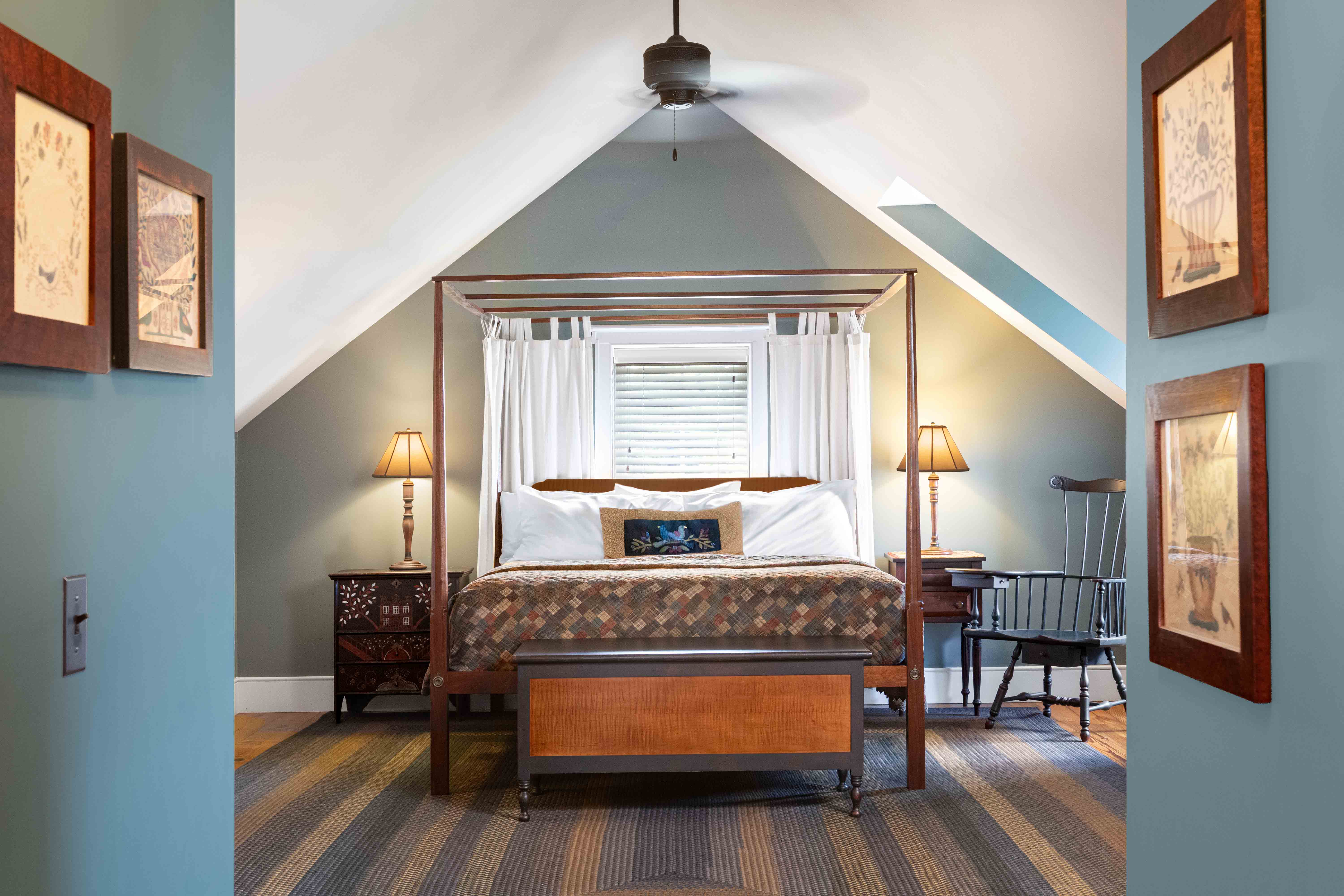 Cozy bedroom with a four-poster bed, soft lighting, and sloped ceilings, accented by framed artwork.
